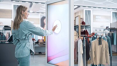 Woman in denim outfit uses an interactive touchscreen in a modern clothing store.