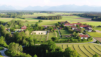 Aerial view of a green landscape with farms, fields, and mountains in the background on a sunny day.