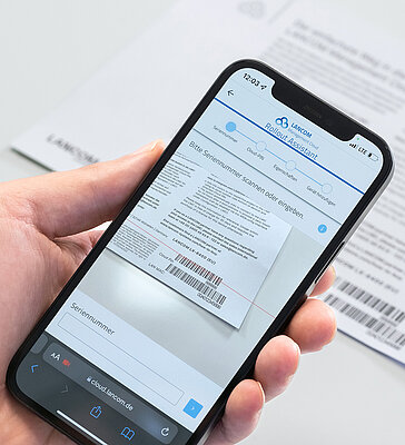 Integrate devices with the Rollout Assistant scan via smartphone into the LMC Hand holds smartphone and uses it to scan barcode from LANCOM cloud-ready enclosure