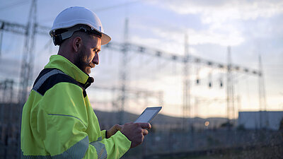 Photograph of middle-aged man with white hard hat and yellow safety vest in front of a power substationLANCOM reference