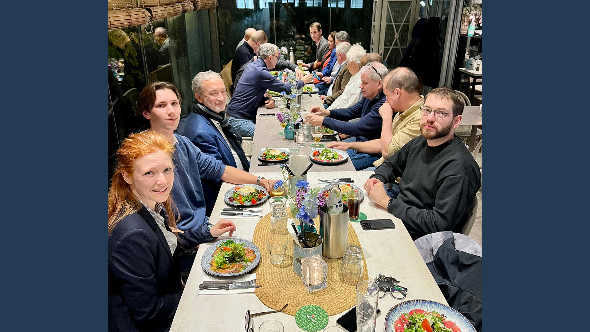 LANCOM event participants sit at a long table enjoying a shared dinner with salads and main courses.