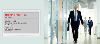 Room signage in the public sector by means of a LANCOM Wireless ePaper Display. A man wearing a suit and carrying a briefcase is walking along a corridor.